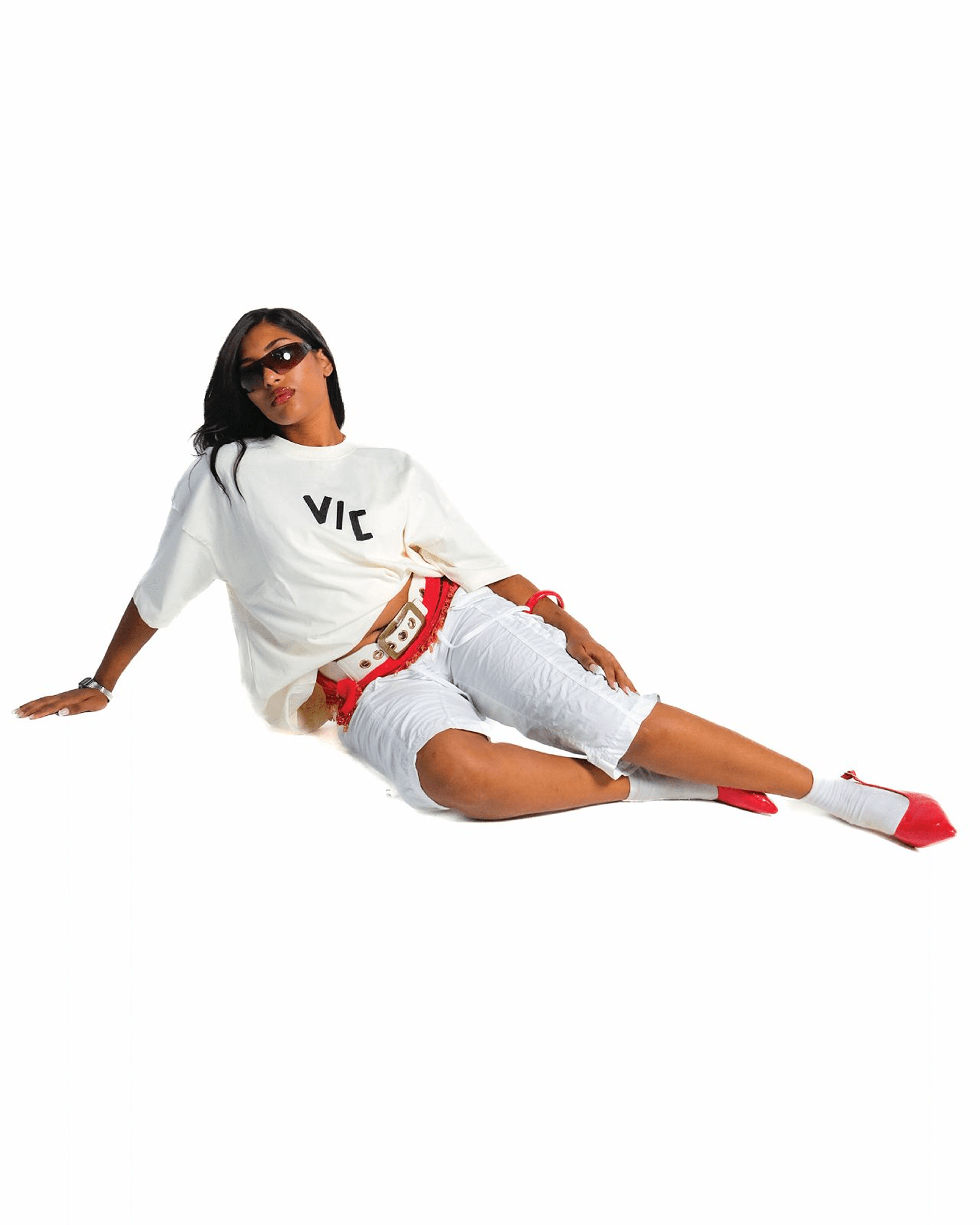 Model seated in a white VIC tee with cargo pants and red heels